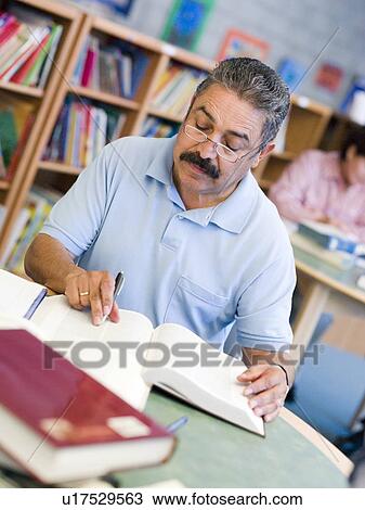 Stock Image - Man sitting in library with a book and notepad (selective focus). Fotosearch