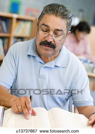 Stock Photo - Man sitting in library with a book and notepad (selective focus). Fotosearch