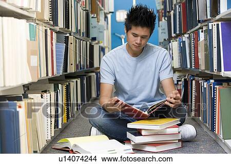 Picture - Man sitting on floor in library reading book. Fotosearch