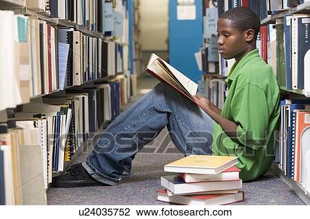 Stock Image - Man sitting on floor in library reading book. Fotosearch