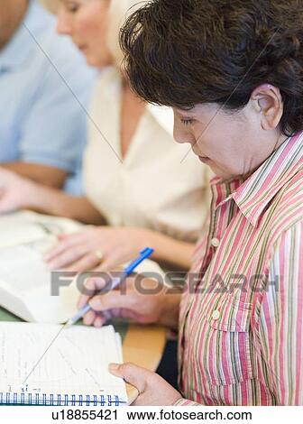 Stock Image - Three people in library with books and notepads (selective focus). Fotosearch