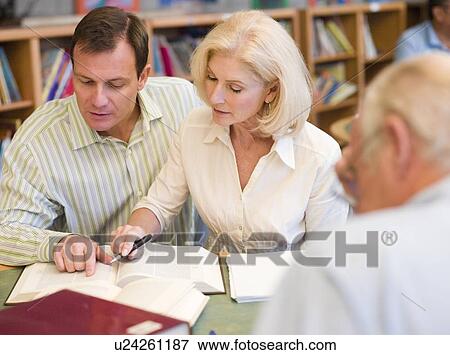 Stock Photo - Three people in library with books and notepads (selective focus). Fotosearch