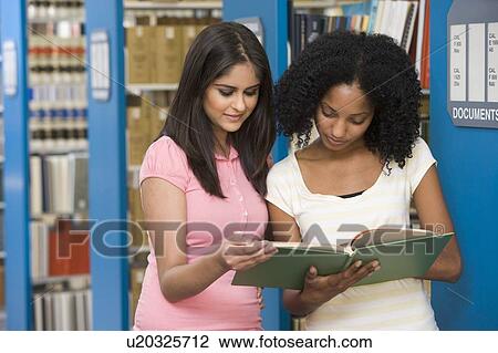 Stock Image - Two women in library reading book (depth of field). Fotosearch