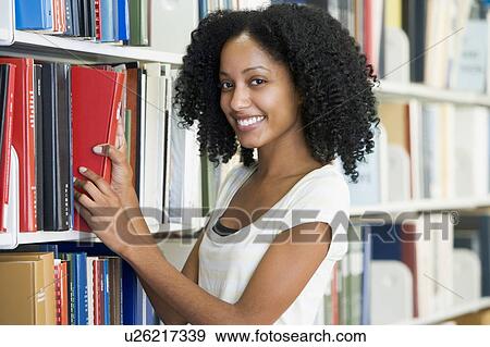 Stock Photo - Woman in library pulling book off a shelf (depth of field). Fotosearch