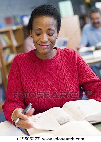 Stock Photo - Woman sitting in library with a book and notepad (selective focus). Fotosearch