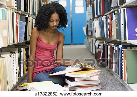 Stock Image - Woman sitting on floor in library reading book. Fotosearch