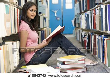 Stock Image - Woman sitting on floor in library holding book. Fotosearch