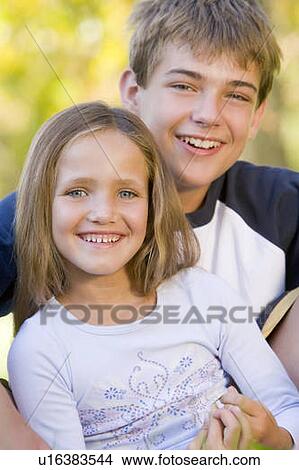 Picture - Brother and sister sitting outdoors smiling. Fotosearch