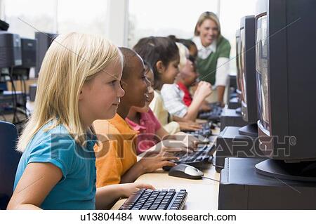 Picture - Children at computer terminals with teacher in background (depth of field/high key). Fotosearch