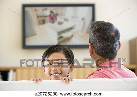 Stock Photo - Man and young boy in living room with flat screen television smiling. Fotosearch
