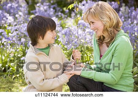 Mother and son outdoors holding flowers smiling View Large Photo Image Picture - Mother and son outdoors holding flowers smiling. Fotosearch