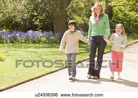 Stock Photograph - Mother and two young children walking on path holding hands smiling. Fotosearch