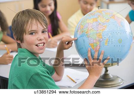 Student in class pointing at globe with students in background (selective focus) View Large Photo Image Picture - Student in class pointing at globe with students in background (selective focus). Fotosearch