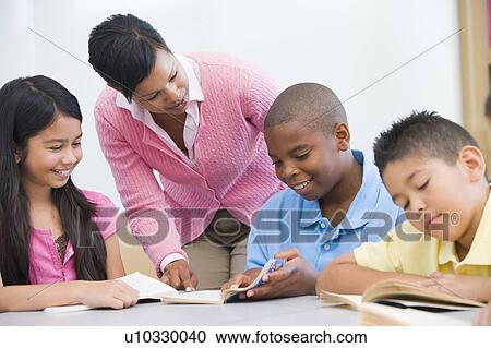 Stock Image - Students in class reading with teacher helping (selective focus). Fotosearch