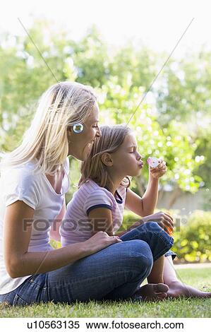 Stock Photography - Woman and young girl outdoors blowing bubbles smiling. Fotosearch