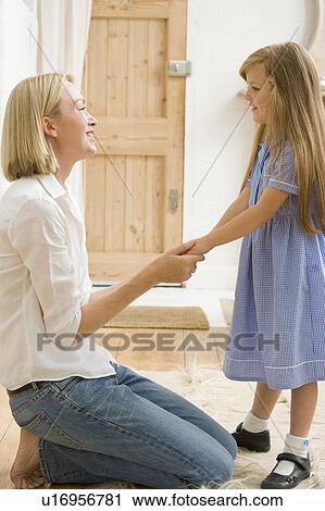 Stock Image - Woman in front hallway holding young girl's hands and smiling. Fotosearch
