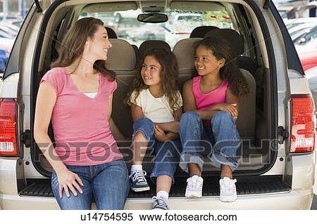Stock Photography - Woman with two young girls sitting in back of van smiling. Fotosearch