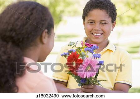 Young boy giving young girl flowers and smiling View Large Photo Image Stock Image - Young boy giving young girl flowers and smiling. Fotosearch