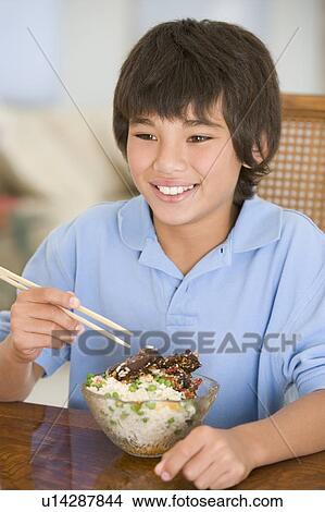 Young boy in dining room eating chinese food smiling View Large Photo Image Picture - Young boy in dining room eating chinese food smiling. Fotosearch