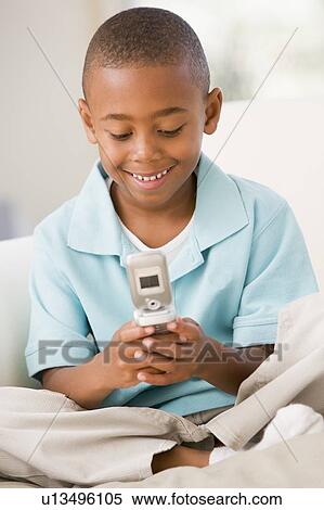 Stock Photography - Young boy in living room using cellular phone and smiling. Fotosearch