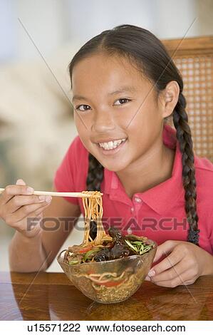 Stock Image - Young girl in dining room eating chinese food smiling. Fotosearch