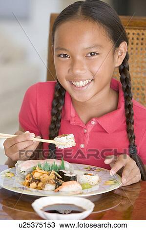 Stock Image - Young girl in dining room eating Chinese food smiling. Fotosearch