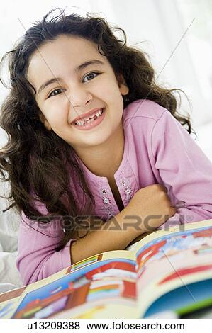 Stock Photo - Young girl in living room with book smiling (high key/selective focus). Fotosearch