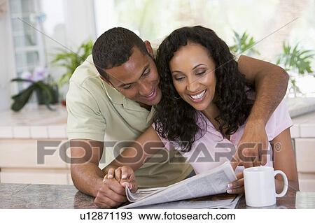 Stock Image - Couple in kitchen with newspaper and coffee smiling. Fotosearch