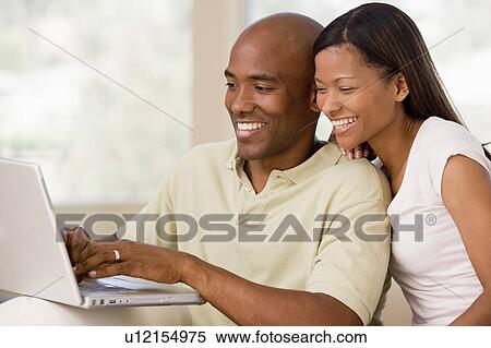 Couple in living room using laptop and smiling View Large Photo Image Stock Photography - Couple in living room using laptop and smiling. Fotosearch
