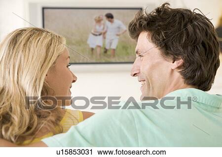 Stock Image - Couple in living room watching television smiling. Fotosearch