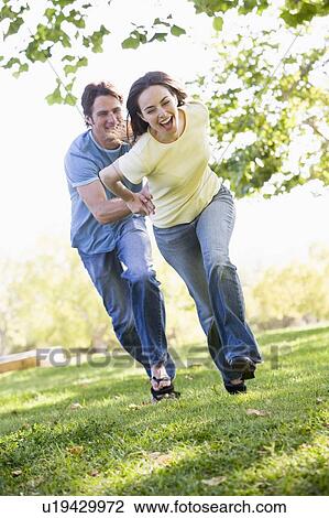 Couple running outdoors holding hands and smiling View Large Photo Image Stock Image - Couple running outdoors holding hands and smiling. Fotosearch