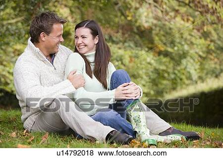 Couple sitting outdoors embracing and smiling (selective focus) View Large Photo Image Stock Photo - Couple sitting outdoors embracing and smiling (selective focus). Fotosearch
