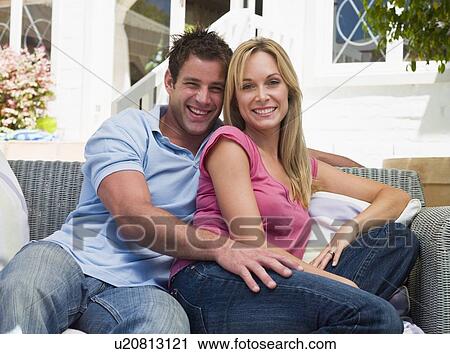 Stock Image - Couple sitting outdoors on patio smiling. Fotosearch