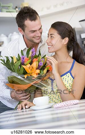 Young man giving a bouquet of flowers to a young girl sitting at a table View Large Photo Image Stock Photograph - Young man giving a bouquet of flowers to a young girl sitting at a table. Fotosearch