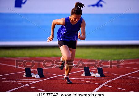 Stock Image - Female athlete running from track starting blocks. Fotosearch