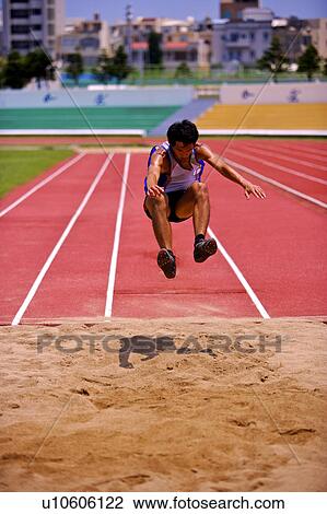 Stock Image - Male athlete long jumping, mid-air. Fotosearch