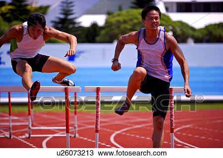 Stock Image - Two male athletes jumping hurdles. Fotosearch