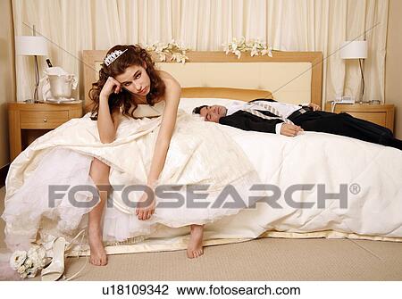 Stock Image - Bride disappointed with groom passed out on hotel bed. Fotosearch
