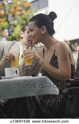 Stock Photo - Business couple in garden cafe drinking orange juice. Fotosearch