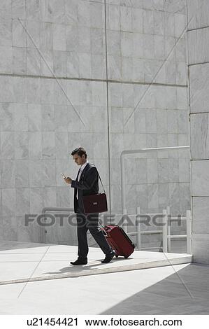 Stock Image - Businessman walking with a suitcase and cell phone. Fotosearch