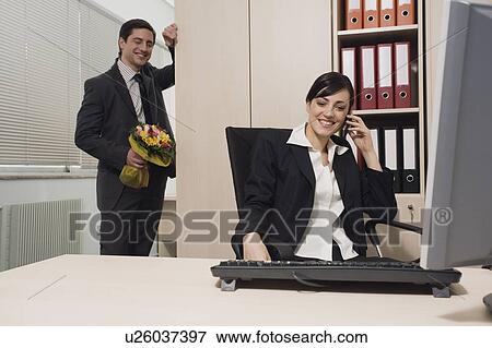 Stock Photo - Male office worker about to surprise female colleague with flowers. Fotosearch