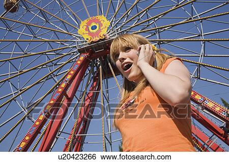 Stock Photograph - Female teenager on cell phone at Ferris wheel in amusement park. Fotosearch