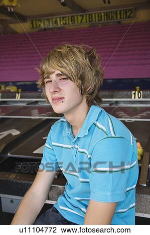 Stock Image - Male teenager posing in front of game in amusement park. Fotosearch