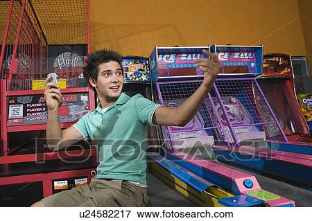 Stock Photo - Male teenager with cell phone in arcade. Fotosearch