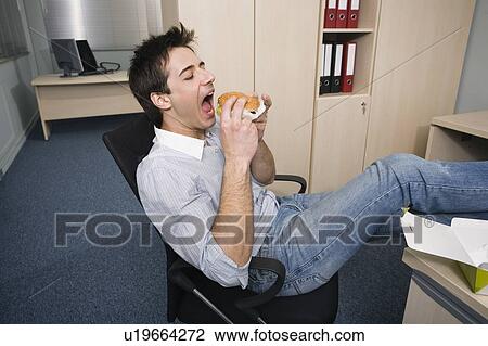 Office worker taking a bite of a hamburger at desk View Large Photo Image Stock Image - Office worker taking a bite of a hamburger at desk. Fotosearch