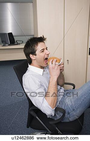 Office worker taking a bite of a hamburger at desk View Large Photo Image Stock Photograph - Office worker taking a bite of a hamburger at desk. Fotosearch