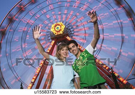 Stock Image - Teenage couple at Ferris wheel in amusement park. Fotosearch