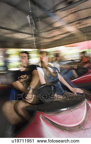 Stock Image - Teenage couple in bumper car in amusement park. Fotosearch