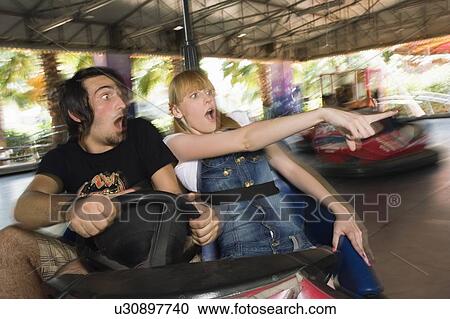 Stock Image - Teenage couple in bumper car in amusement park. Fotosearch