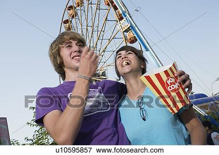 Stock Photo - Teenage couple in front of Ferris wheel in amusement park. Fotosearch